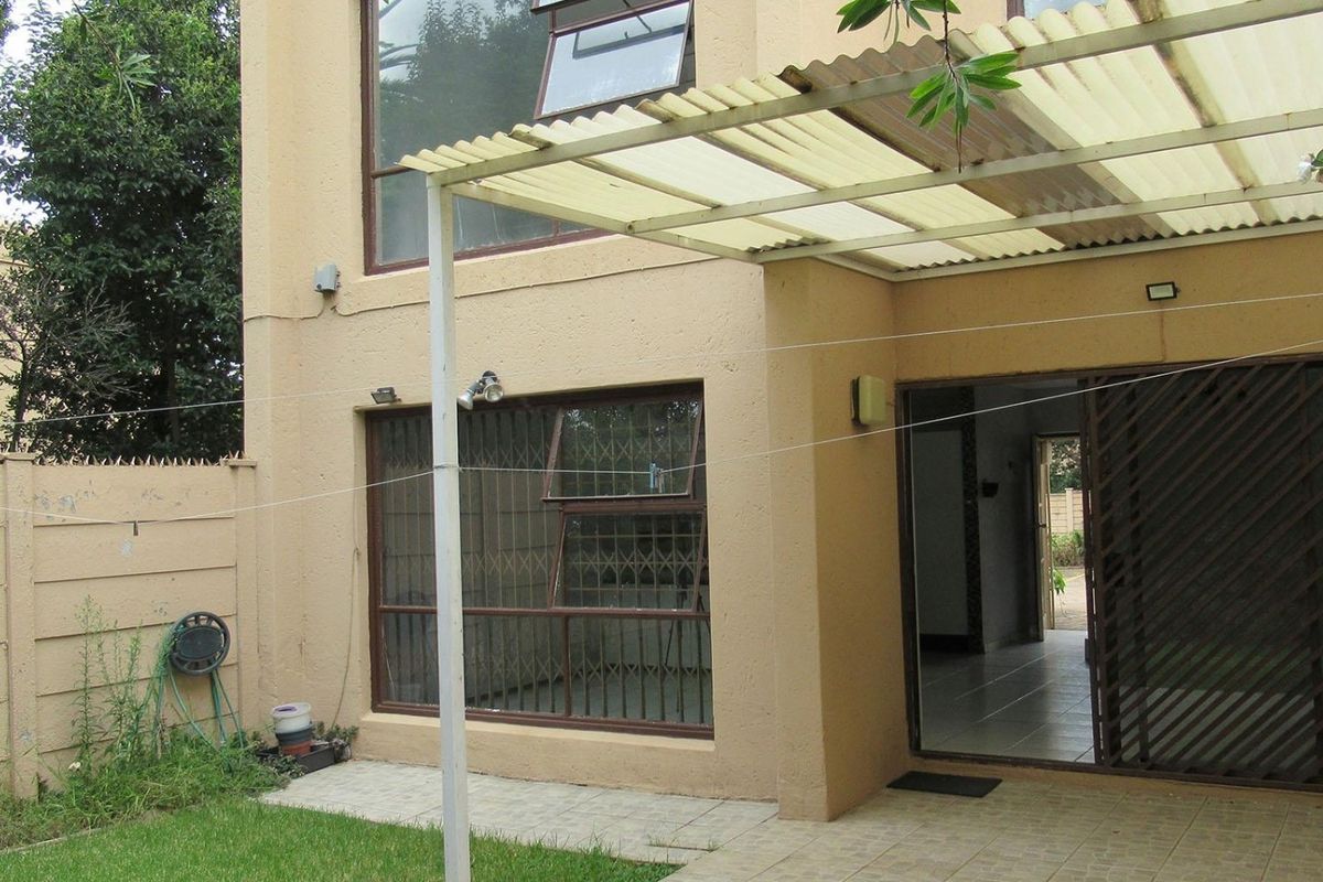 Rear view of the townhouse featuring a paved patio area with a corrugated roof, security bars on windows, and a small private garden space.