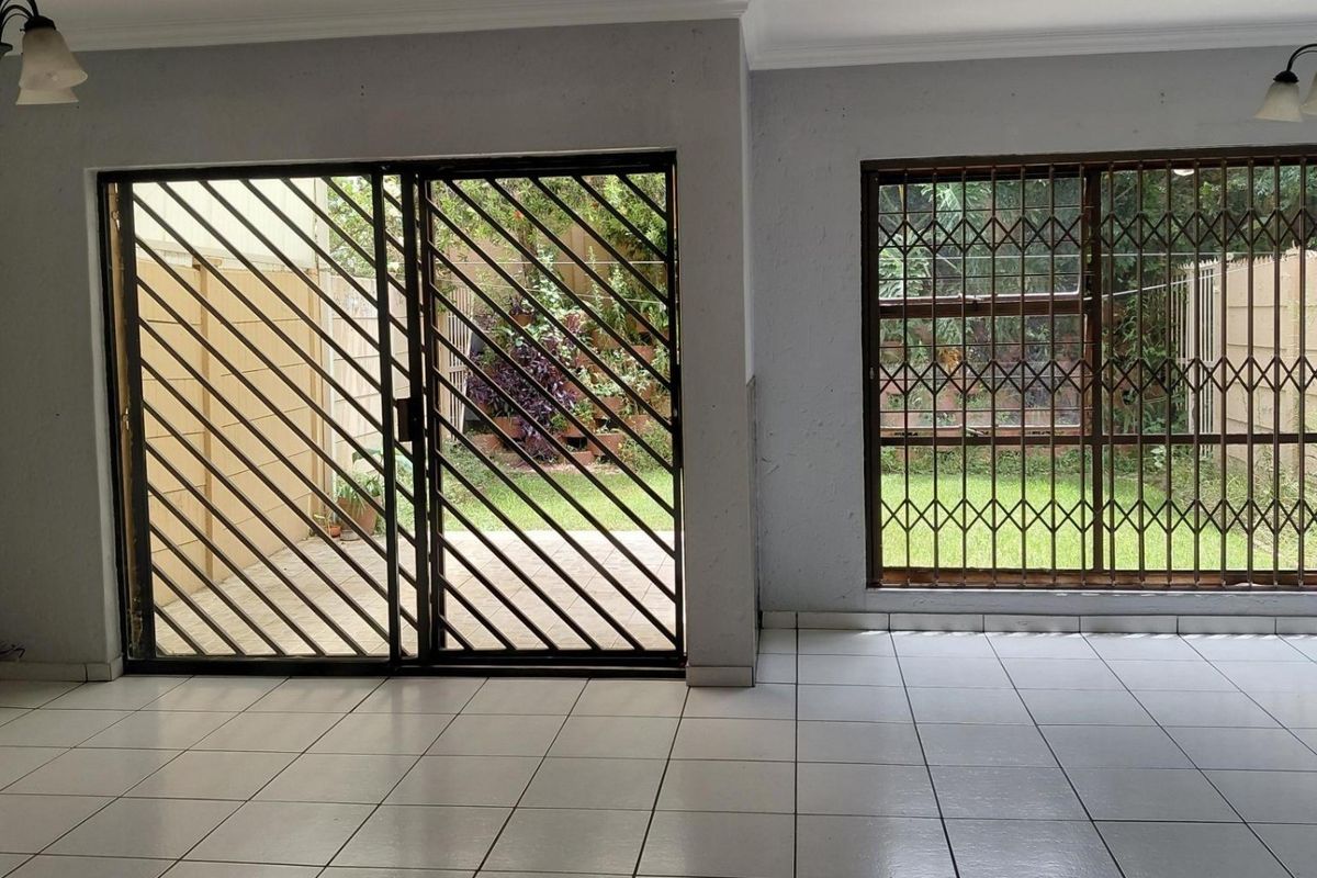 Spacious living area featuring ceramic floor tiles, sliding glass doors with security gates, and large windows with security bars overlooking the garden.