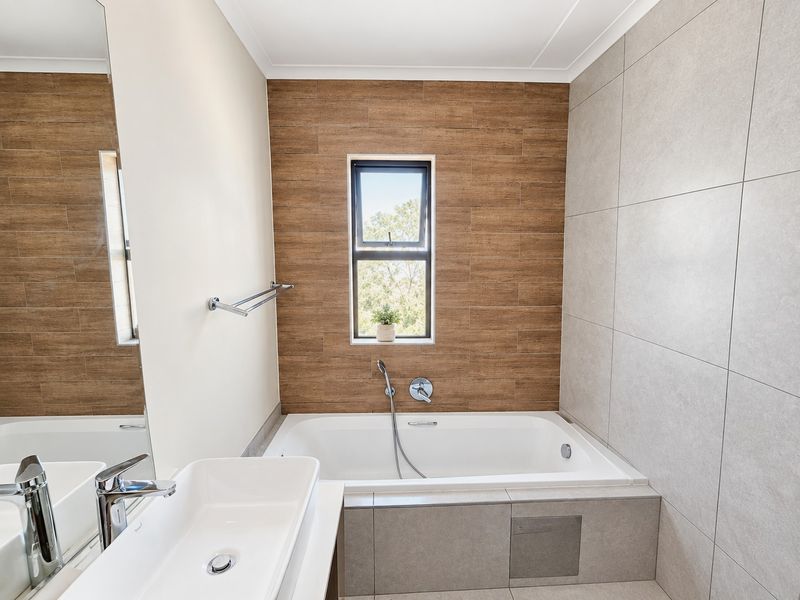 Modern bathroom featuring a built-in bathtub, vessel sink, large mirror, and contemporary wood-look and neutral ceramic tiling.