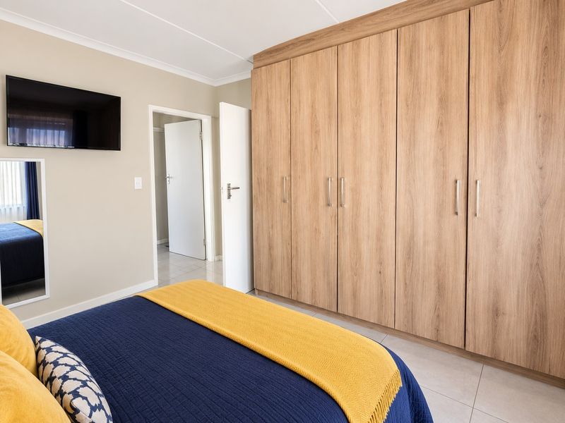 A well-maintained bedroom featuring extensive light wood-finish built-in cupboards, neutral wall tones, and clean tiled flooring.