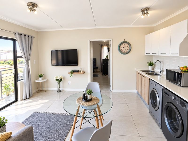 Bright open-plan living area featuring a modern kitchen with integrated laundry, tiled floors, and a sliding door leading to a balcony.