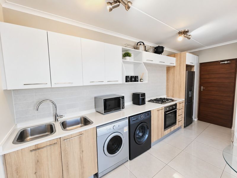 Modern kitchen featuring light wood-grain cabinetry, white upper cabinets, integrated appliances, gas hob, oven, and sleek tiled splashback with porcelain flooring.