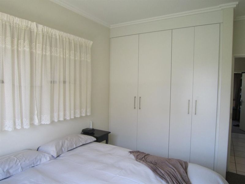 A bedroom featuring neutral walls, built-in cupboards, and a window with curtains.