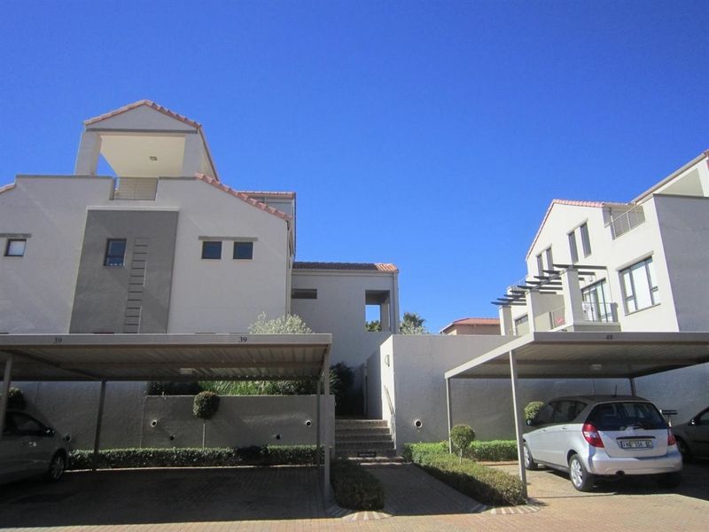 Front view of the apartment complex featuring covered parking bays, paved access paths, and multi-level building architecture with balconies.