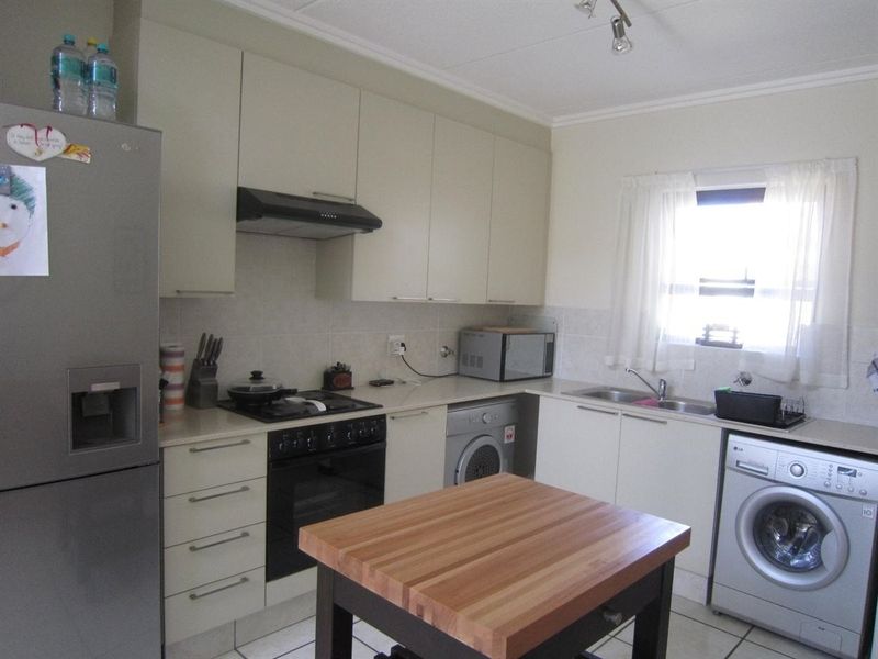 A functional kitchen featuring built-in cabinetry, a gas hob with extractor, integrated oven, and a double sink with tiled flooring and backsplash.