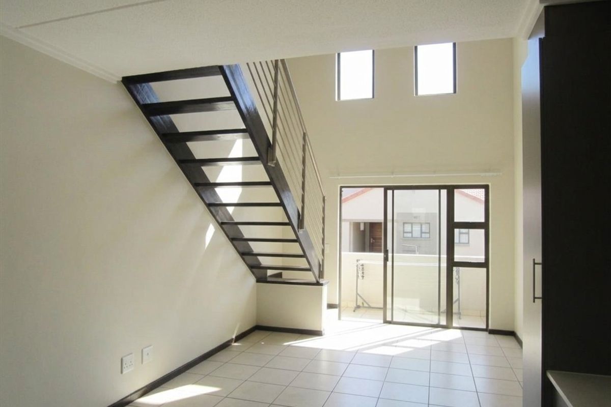 Bright and spacious open-plan living area featuring a modern staircase, tiled flooring, and large sliding glass doors leading to an outdoor balcony.