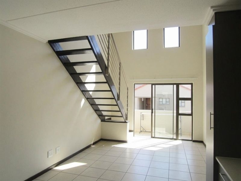 Bright and spacious open-plan living area featuring a modern staircase, tiled flooring, and large sliding glass doors leading to an outdoor balcony.