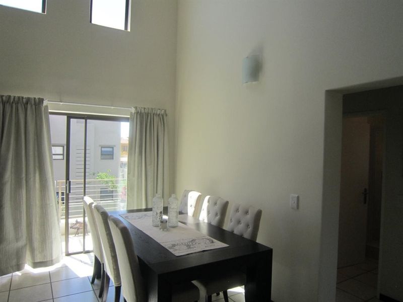Dining area featuring double-height ceilings, tiled flooring, and a sliding glass door providing access to an outdoor balcony.