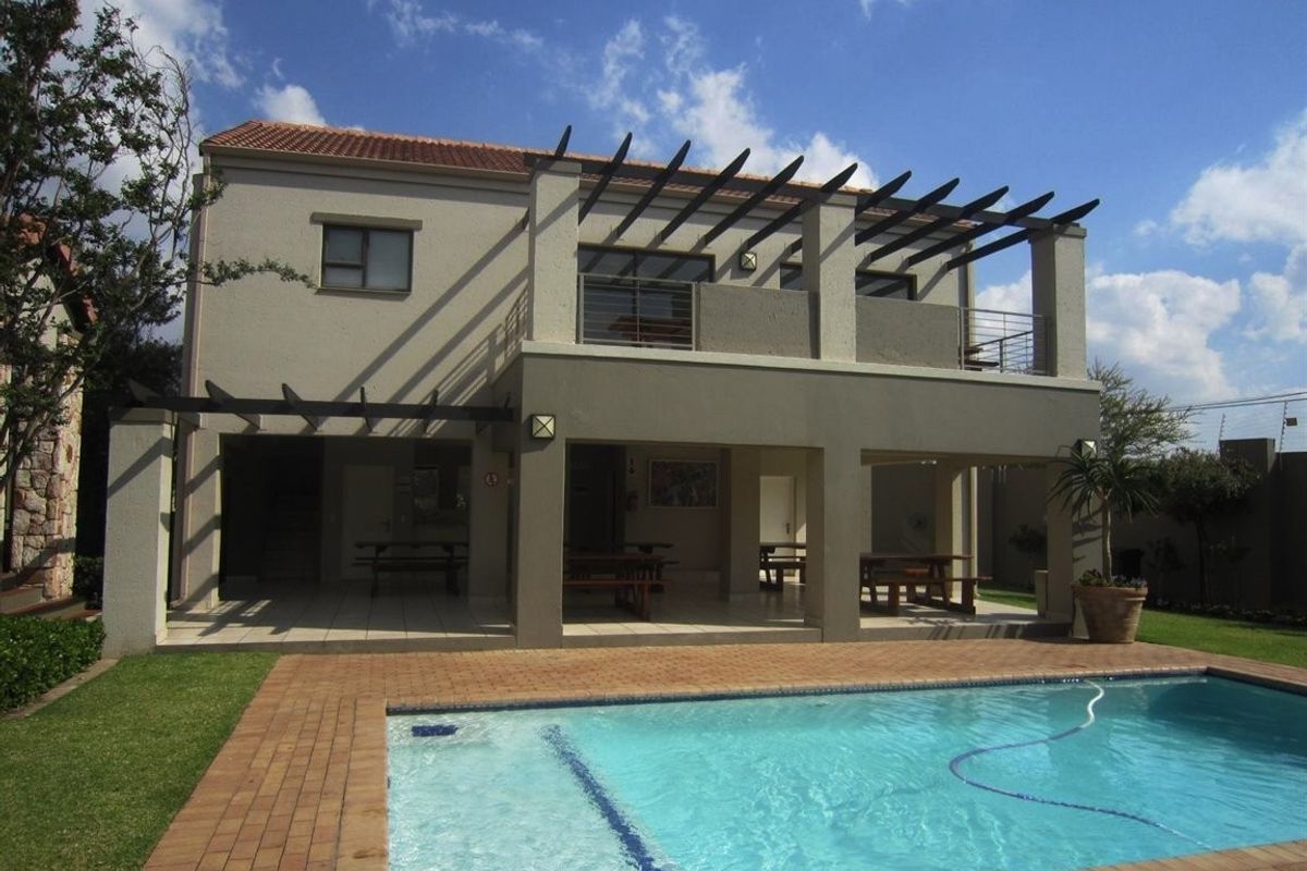 Rear view of a two-story apartment building featuring a swimming pool, paved pool deck, and a covered patio with an overhead balcony and pergola.