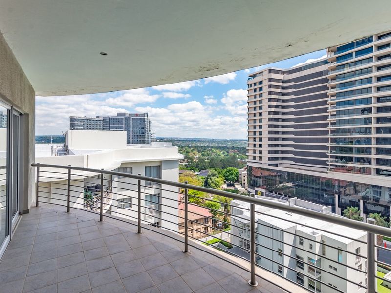 A spacious covered balcony featuring tiled flooring and a modern stainless steel balustrade, offering expansive urban views.