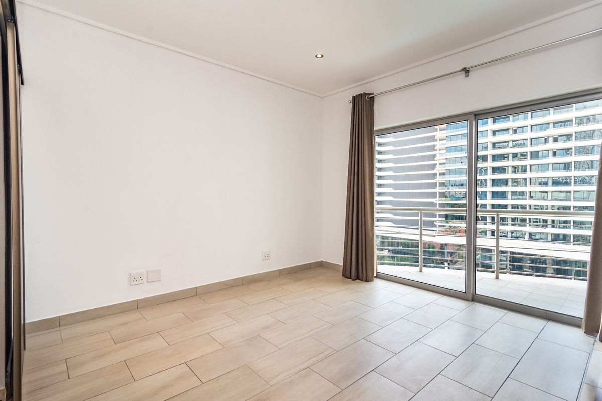 A bright, empty bedroom featuring modern tiled flooring, recessed lighting, and a large sliding glass door providing access to a private balcony.