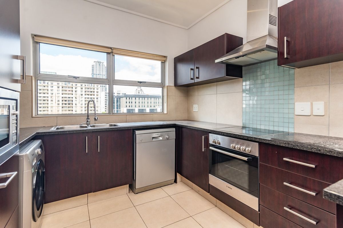 A well-maintained kitchen featuring dark wood cabinetry, granite countertops, integrated stainless steel appliances, and a tiled splashback with ample natural light.