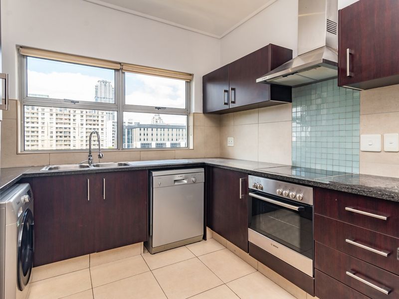 A well-maintained kitchen featuring dark wood cabinetry, granite countertops, integrated stainless steel appliances, and a tiled splashback with ample natural light.