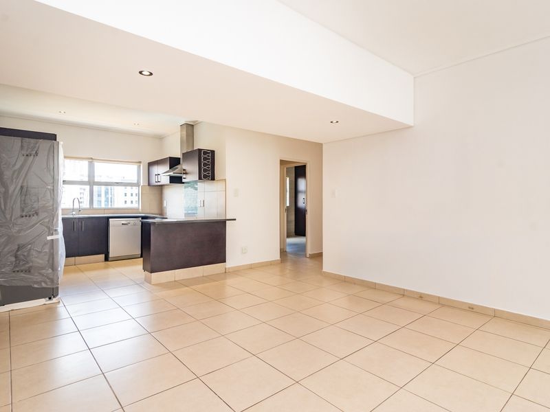 An open-plan living and kitchen area featuring neutral tiled flooring, modern cabinetry, and a breakfast counter, offering a bright and versatile living space.