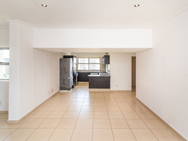 An open-plan living and kitchen area featuring neutral tiled flooring, recessed lighting, and a functional kitchen layout with built-in cabinetry and a central island.