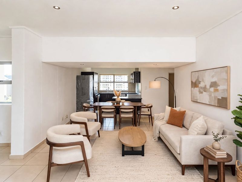 A bright open-plan living and dining area featuring neutral tiled flooring, recessed lighting, and a functional kitchen space with modern cabinetry.