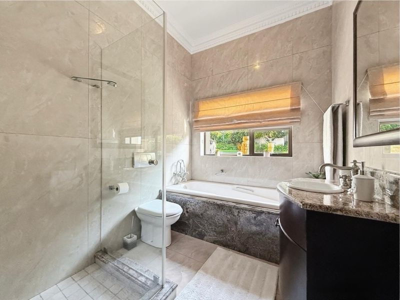 Modern bathroom featuring a glass-enclosed shower, built-in bathtub, granite vanity, and neutral floor-to-ceiling tiling.