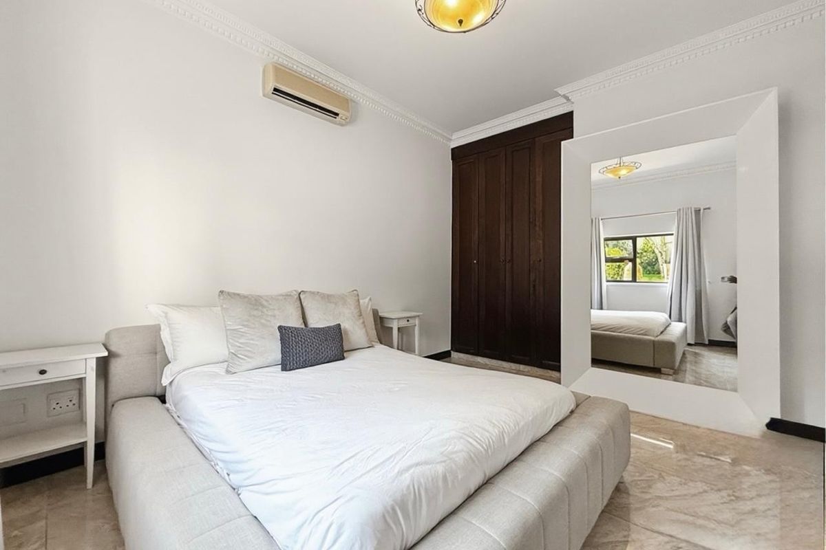 A well-maintained bedroom featuring built-in dark wood cupboards, tiled flooring, decorative ceiling cornicing, and a wall-mounted air conditioning unit.