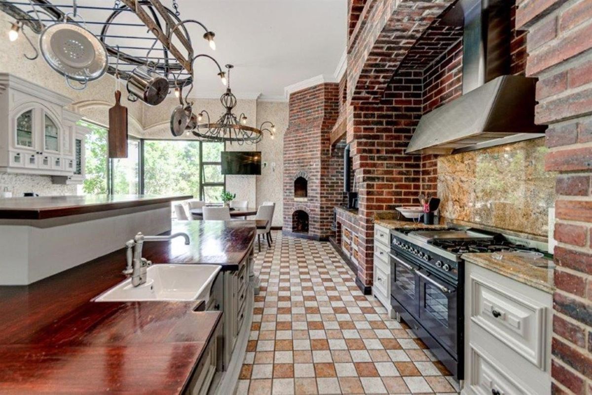 Spacious kitchen featuring a prominent brick fireplace, farmhouse sink, wooden countertops, and a professional-style gas range with an integrated extractor fan.