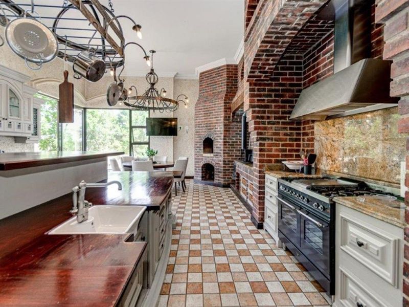 Spacious kitchen featuring a prominent brick fireplace, farmhouse sink, wooden countertops, and a professional-style gas range with an integrated extractor fan.