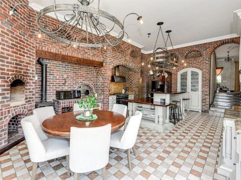 Spacious open-plan kitchen and dining area featuring rustic exposed brick walls, arched architectural details, a central kitchen island, and classic tiled flooring.