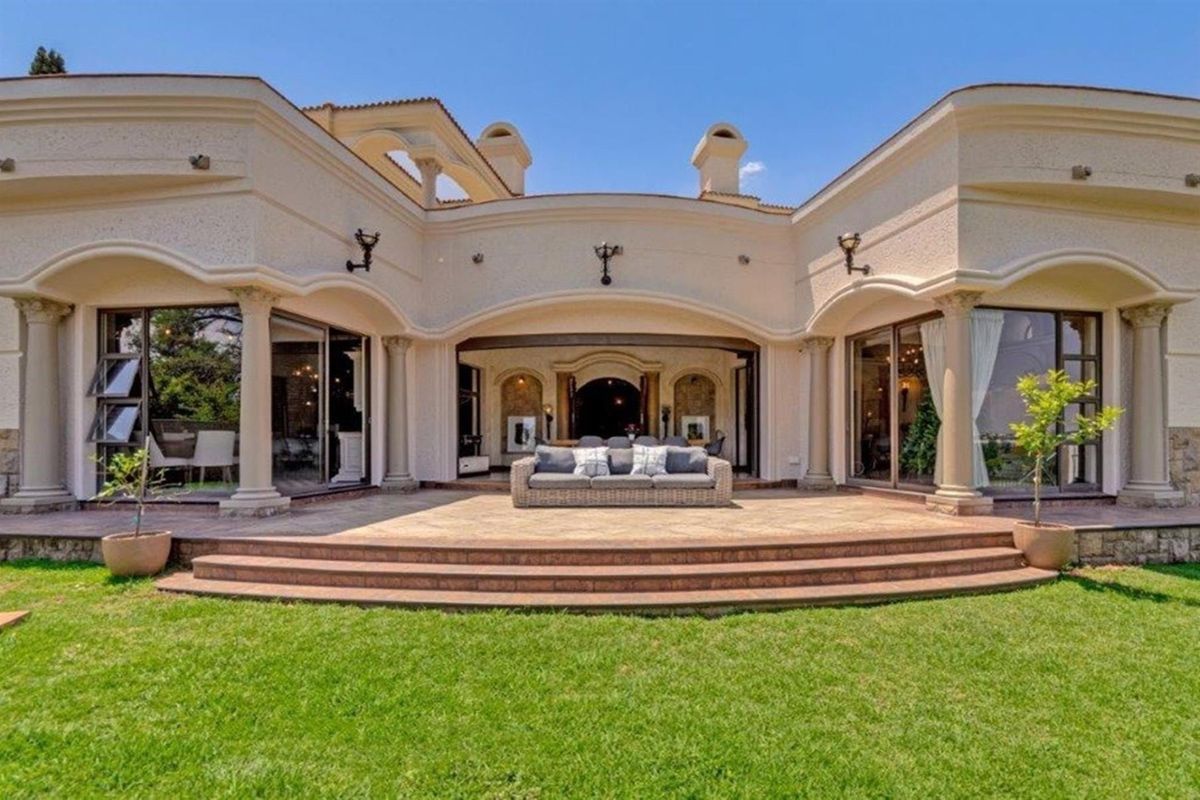 Spacious rear patio featuring elegant curved architecture, decorative columns, and large sliding glass doors opening into the home, overlooking a well-maintained garden.
