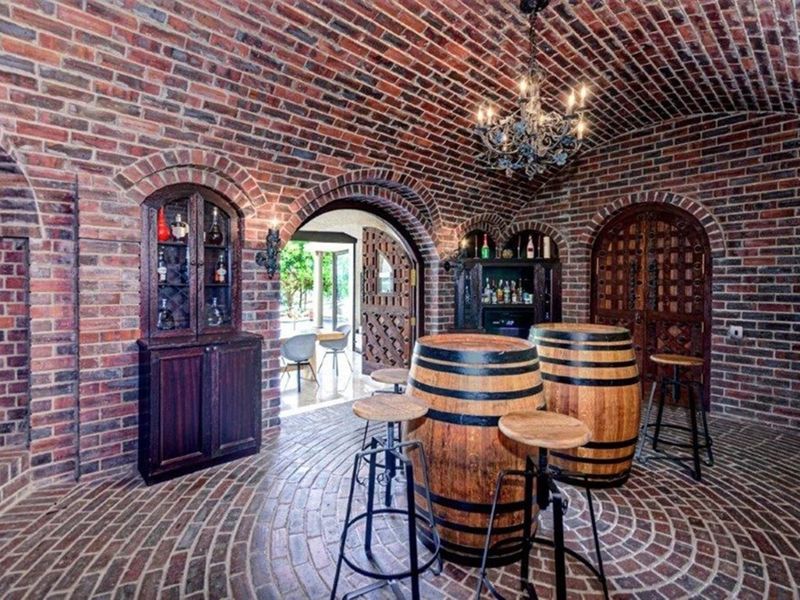 A rustic wine cellar featuring a distinctive brick barrel vaulted ceiling, intricate brickwork flooring, and custom arched wooden doorways.