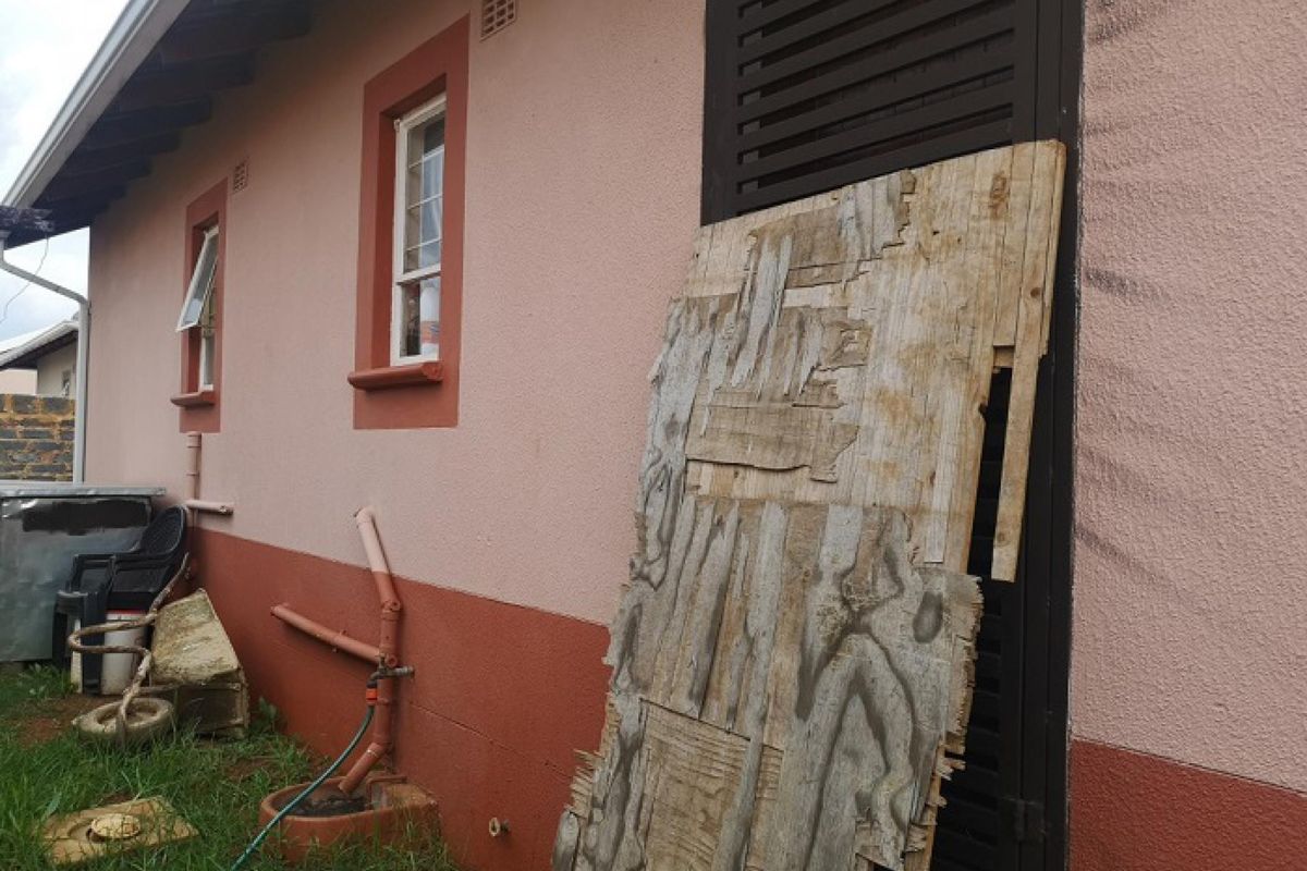 Rear exterior view of the house showing a damaged door covering, exposed plumbing, and painted masonry walls.