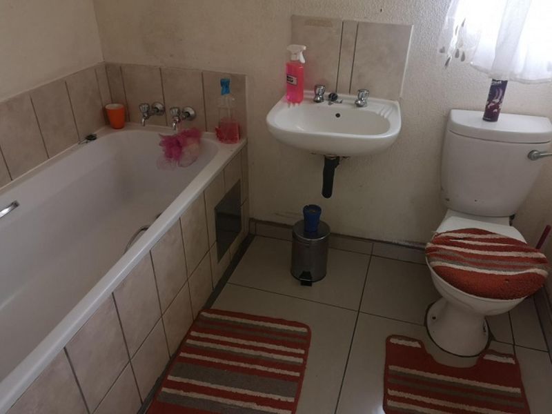 A functional bathroom featuring a standard bathtub, wall-mounted basin, and toilet with tiled finishes, requiring cosmetic updates to improve its overall condition.