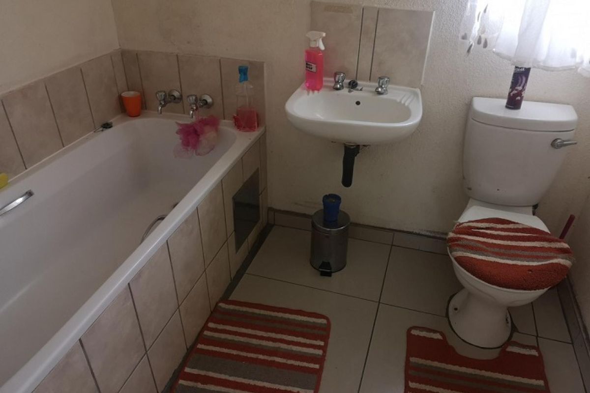 A functional bathroom featuring a standard bathtub, wall-mounted basin, and toilet with tiled finishes, requiring cosmetic updates to improve its overall condition.
