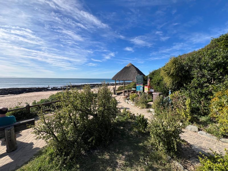 Scenic coastal view featuring a thatched gazebo, paved pathways, and direct access to the beach and ocean.