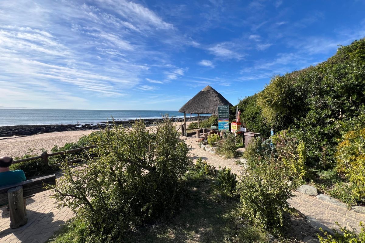 Scenic coastal view featuring a thatched gazebo, paved pathways, and direct access to the beach and ocean.