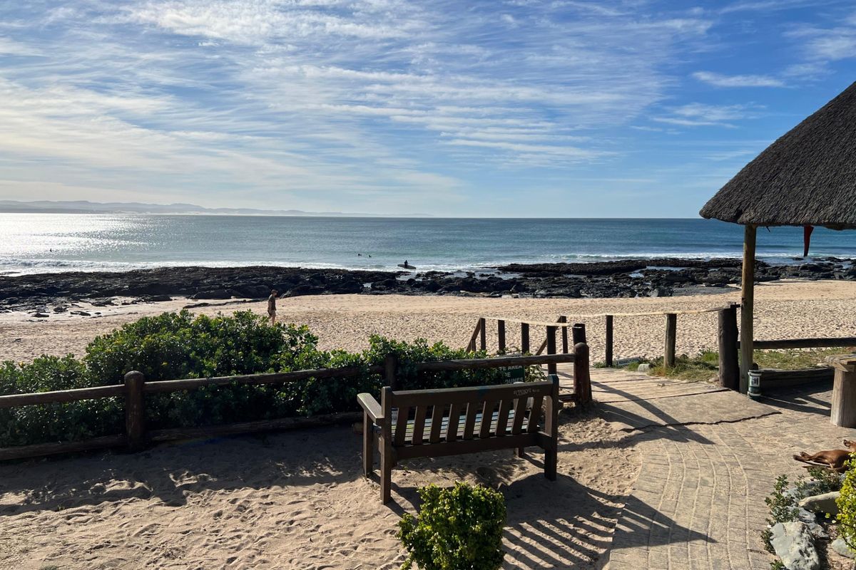 Scenic coastal view overlooking the beach and ocean, featuring a thatched roof structure and paved pathway access.