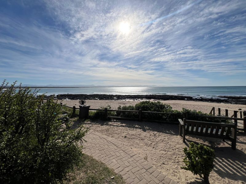 A scenic view overlooking the coastline, featuring a paved walkway and timber fencing leading towards the beach and ocean.