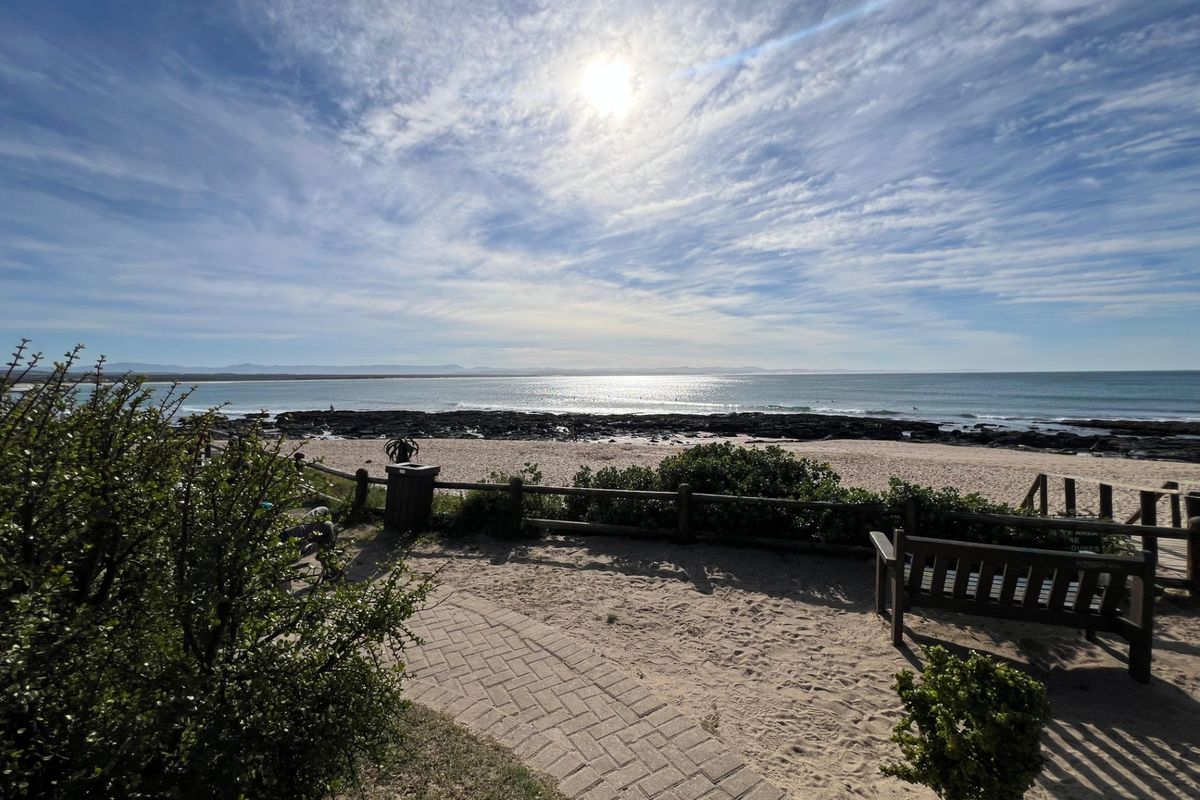 A scenic view overlooking the coastline, featuring a paved walkway and timber fencing leading towards the beach and ocean.