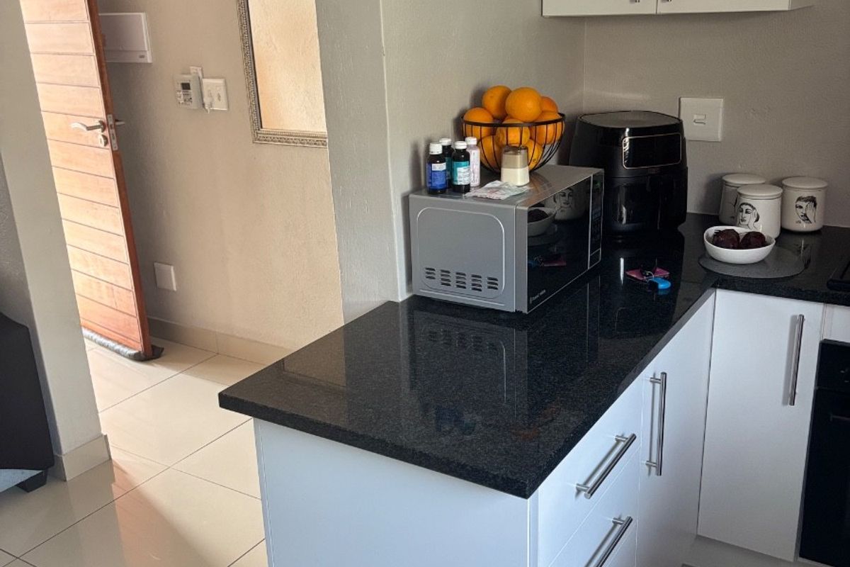 A modern kitchen featuring white cabinetry, sleek black granite countertops, and neutral tiled flooring, seamlessly connected to the adjacent hallway.