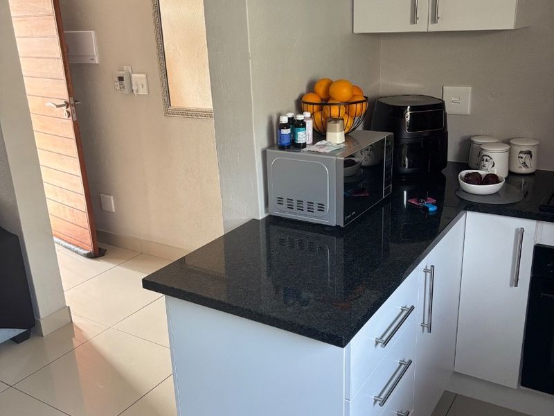 A modern kitchen featuring white cabinetry, sleek black granite countertops, and neutral tiled flooring, seamlessly connected to the adjacent hallway.