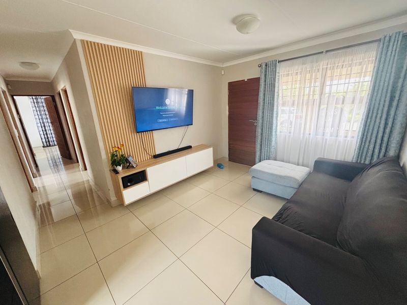 A well-maintained living room featuring large format floor tiles, a modern timber slat feature wall, and a built-in media console.