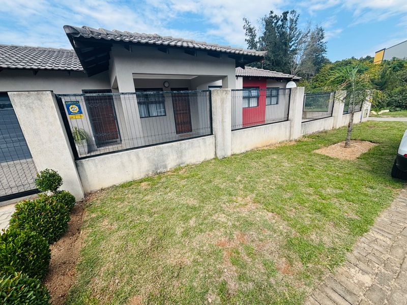 Front exterior view of the house featuring a concrete boundary wall, wire mesh fencing, tiled roof, and a paved driveway.