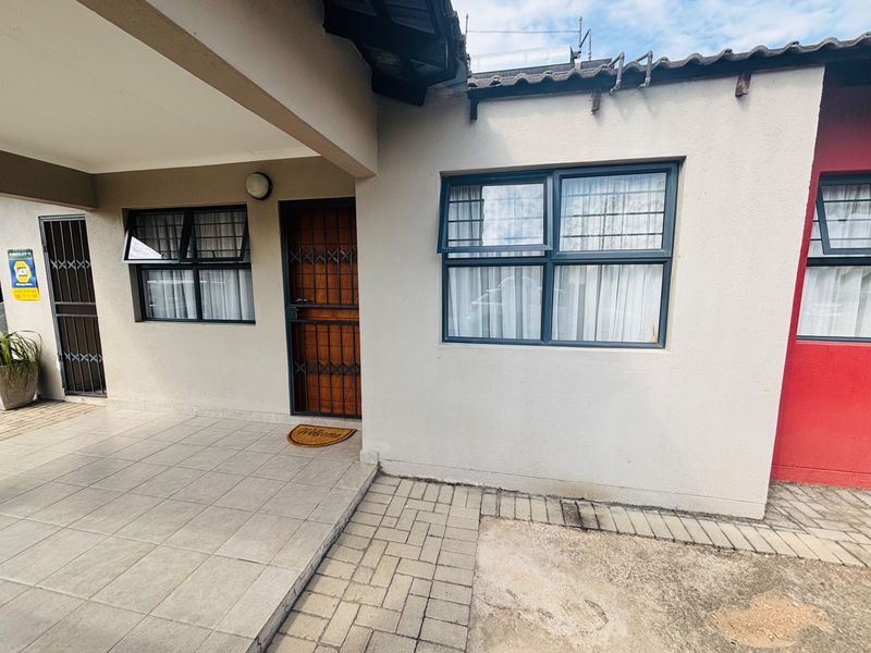 Front entrance area featuring a tiled patio, security gate, and paved driveway access.