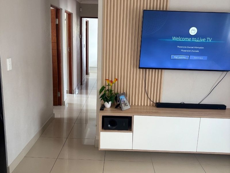 A modern living area featuring a decorative slatted timber feature wall, neutral tiled flooring, and a clean, contemporary layout leading into a hallway.