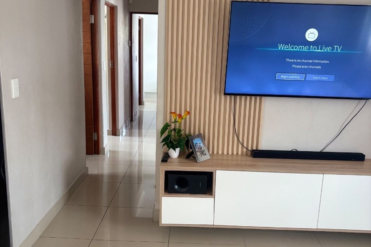 A modern living area featuring a decorative slatted timber feature wall, neutral tiled flooring, and a clean, contemporary layout leading into a hallway.
