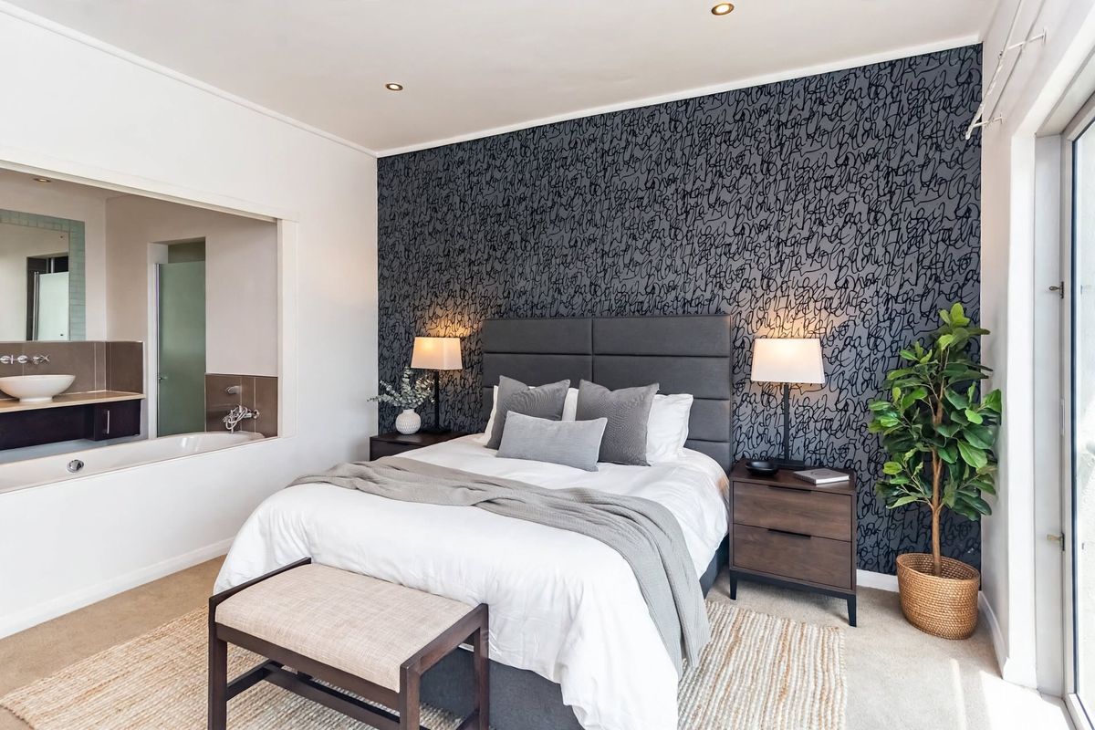 A well-appointed bedroom featuring a modern accent wall, recessed lighting, and an open-plan en-suite bathroom with a soaking tub.