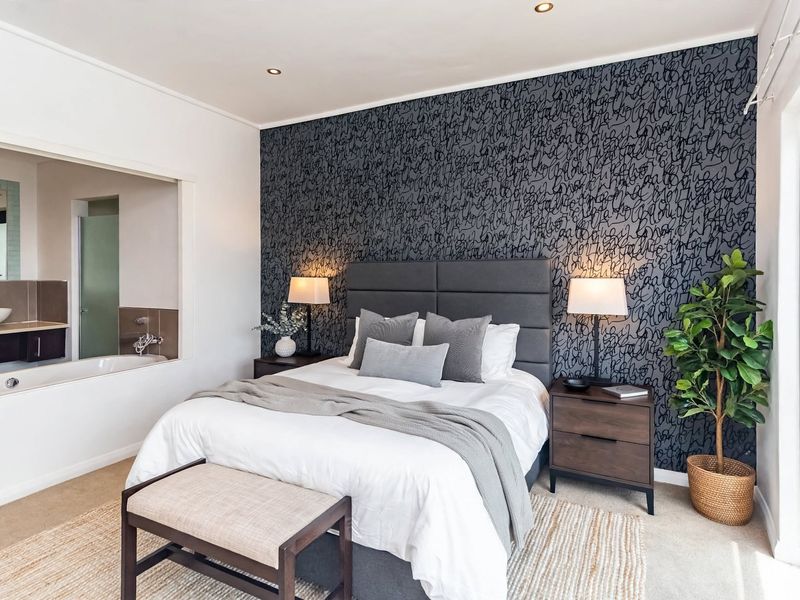 A well-appointed bedroom featuring a modern accent wall, recessed lighting, and an open-plan en-suite bathroom with a soaking tub.