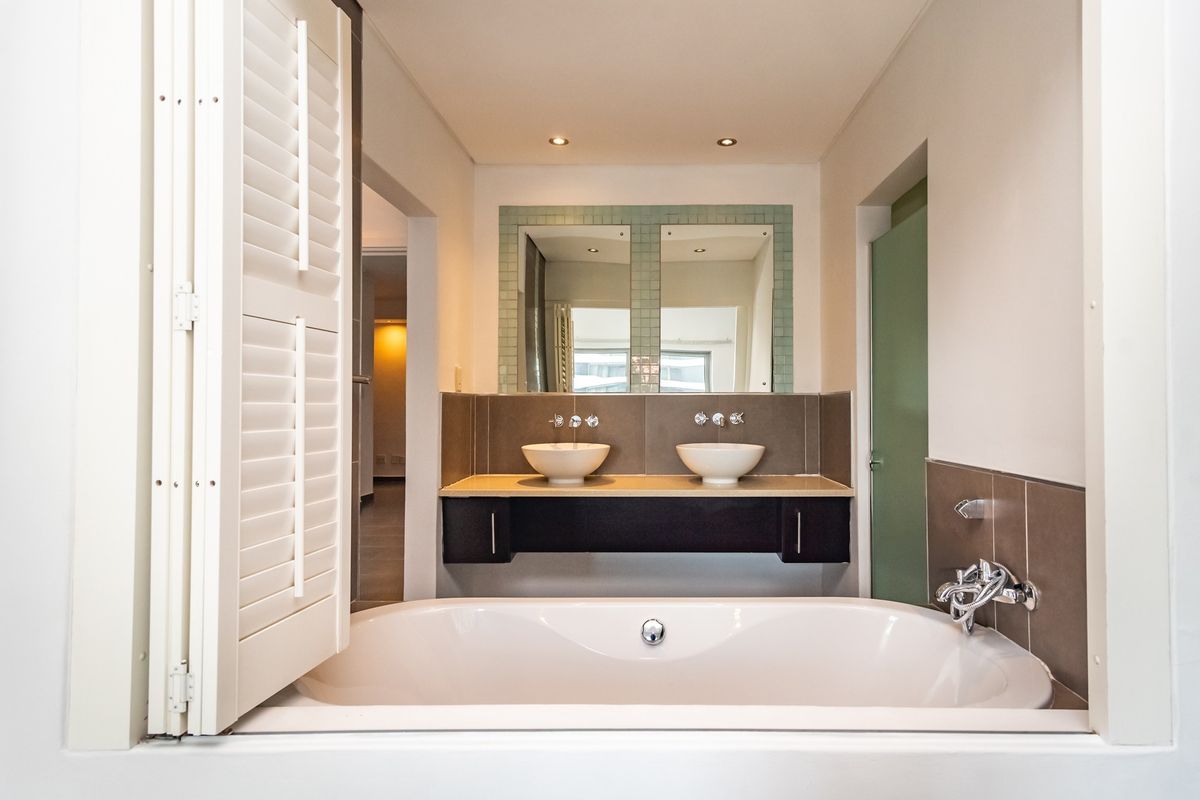A modern bathroom featuring a double vanity with vessel sinks, a built-in bathtub, and elegant wall-mounted faucets, finished with clean, neutral tiling.