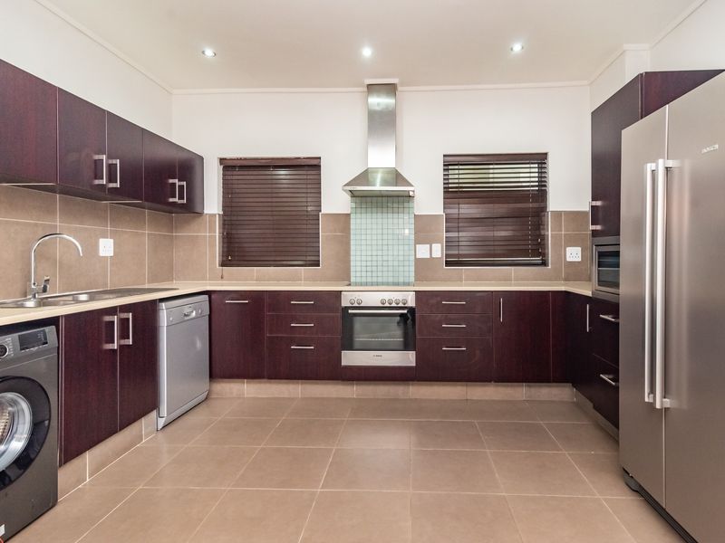 Modern kitchen featuring dark wood cabinetry, stainless steel appliances, tiled backsplash, and neutral floor tiles with ample storage and workspace.