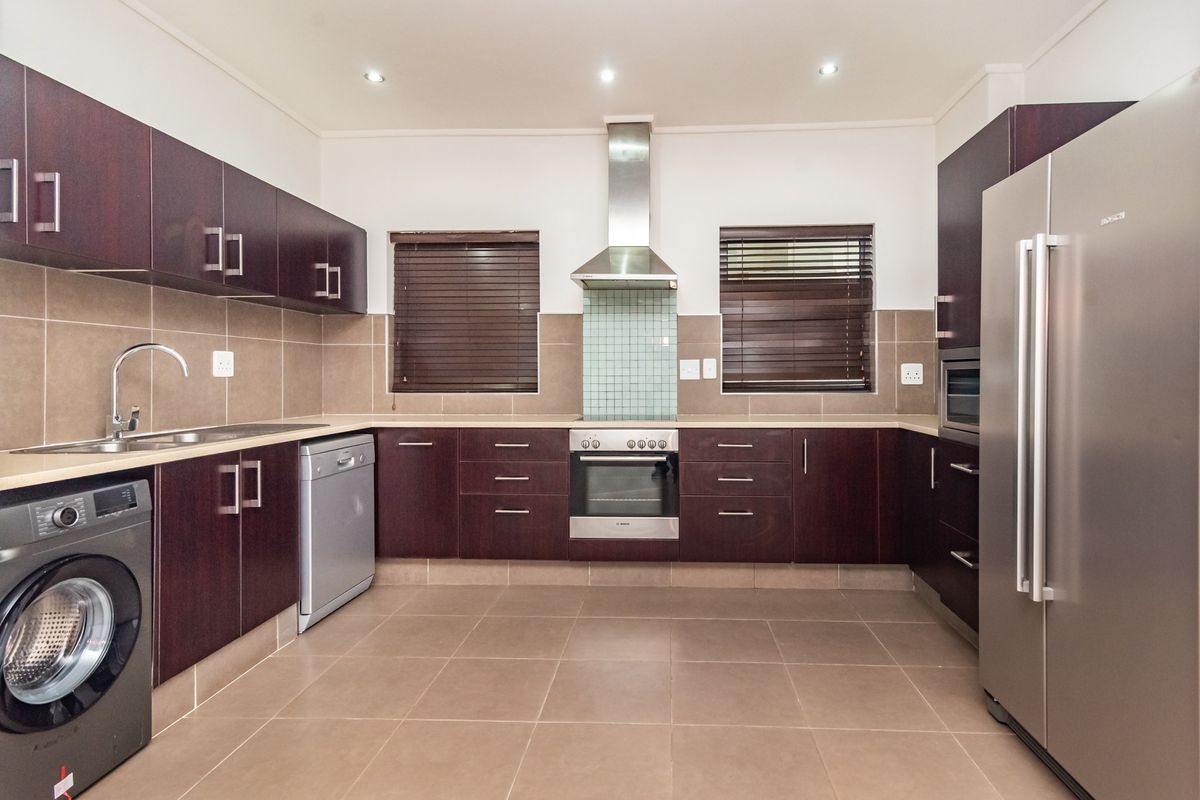Modern kitchen featuring dark wood cabinetry, stainless steel appliances, tiled backsplash, and neutral floor tiles with ample storage and workspace.