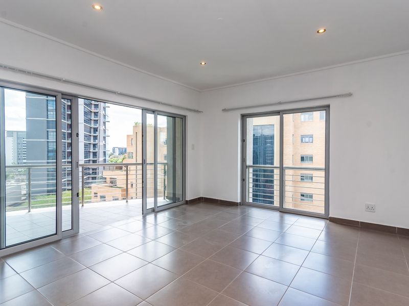 Spacious, light-filled living area featuring neutral tiled flooring, recessed lighting, and large sliding glass doors opening onto a private balcony with urban views.