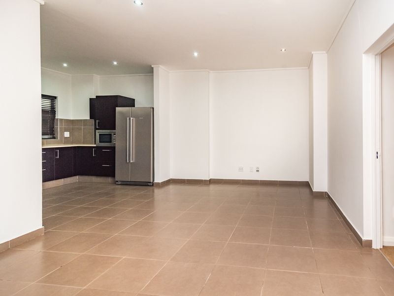 Spacious open-plan living area featuring neutral tiled flooring, recessed lighting, and a modern kitchen with built-in cabinetry and integrated appliances.
