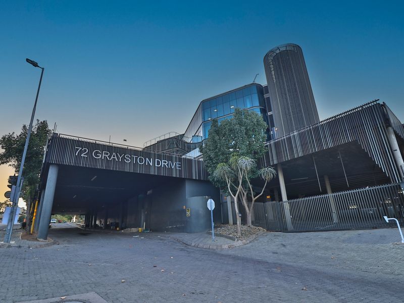 Modern commercial building facade at 72 Grayston Drive featuring glass curtain walls, metal louvers, and a paved driveway entrance.